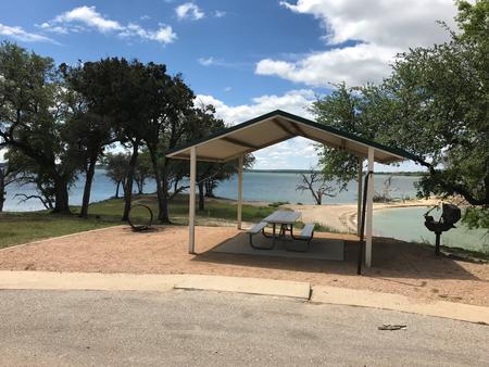 Covered picnic table, grill, and fire ring with Waco Lake in the background