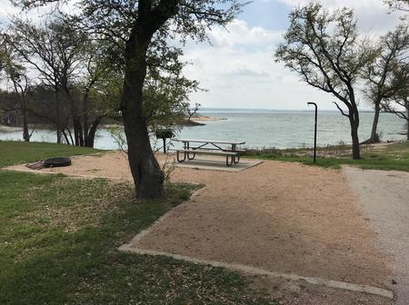 Picnic table, grill, and fire ring with Waco Lake in the background