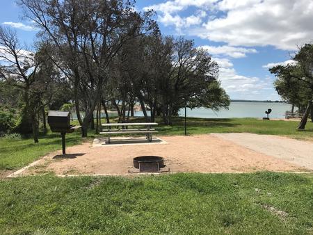 Picnic table, grill, and fire ring with Waco Lake in the background