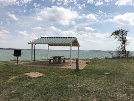 Tent site with covered picnic table, grill, and fire ring.  Site is located very close to shoreline of Waco Lake