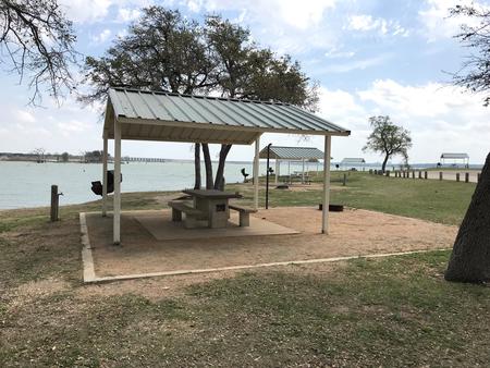 Tent site with covered picnic table, grill, and fire ring.  Site is located very close to shoreline of Waco Lake