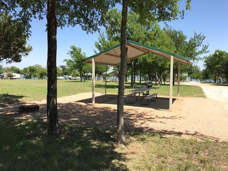 Covered picnic table, grill, and fire ring at site with Waco Lake in the background