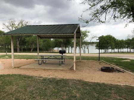 RV site with covered picnic table, grill, fire ring, and Waco Lake in the background