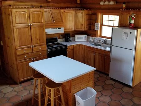 View of the kitchen in the Hillside Cabin with wood cabinents refrig, stove, and island bar with 2 stoolsHillside Cabin kitchen