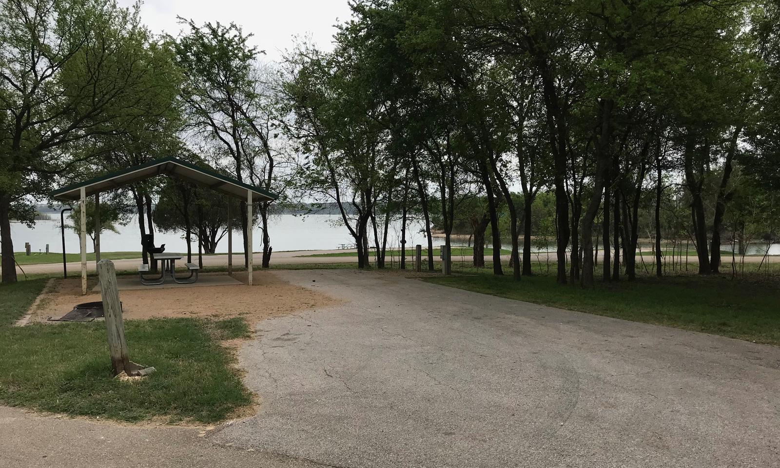 RV site with covered picnic table, grill, fire ring, and Waco Lake in the background