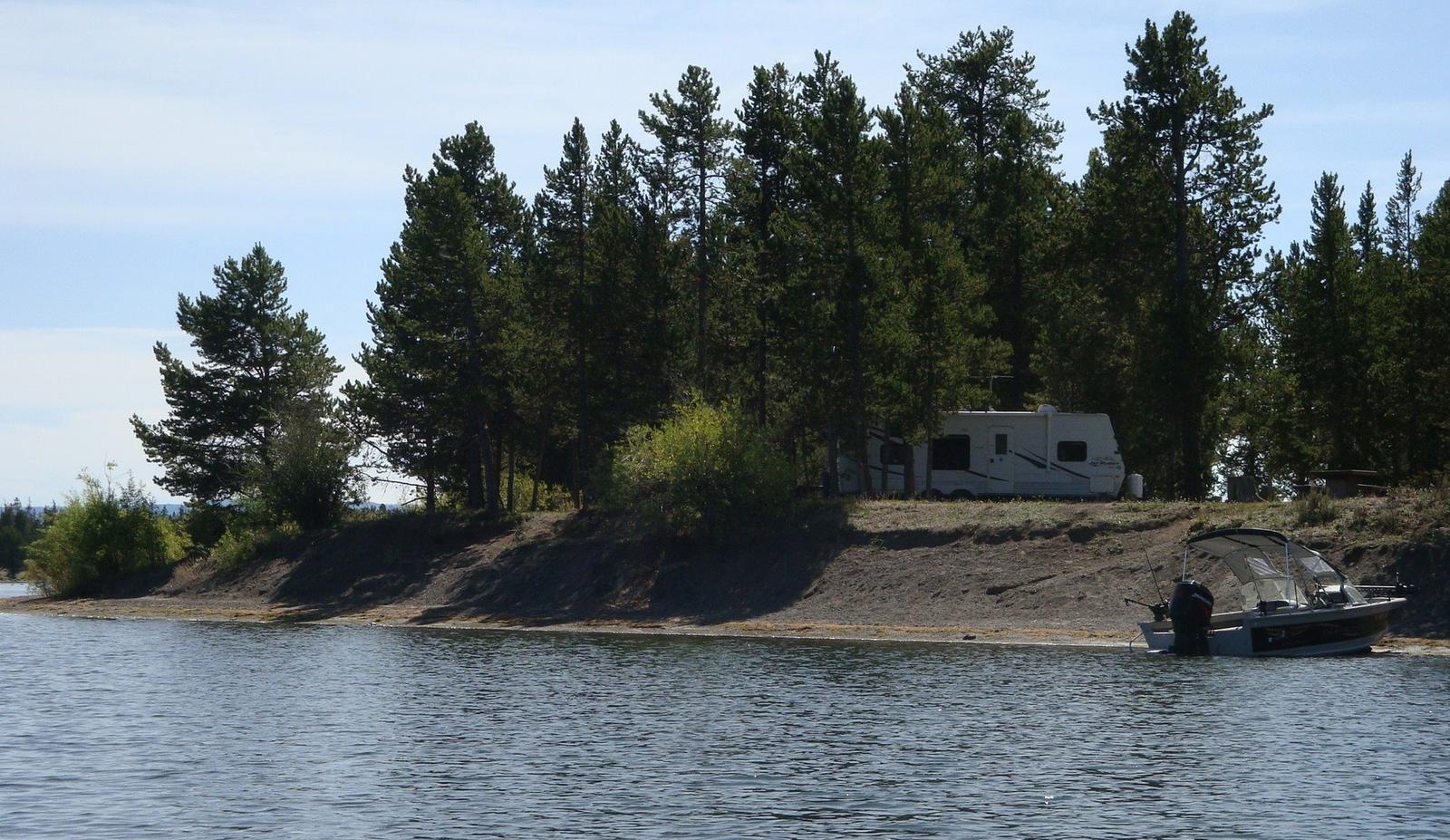 View from Hebgen Lake - Lake, boat and RV surrounded by pine treesLonesomehurst Campground