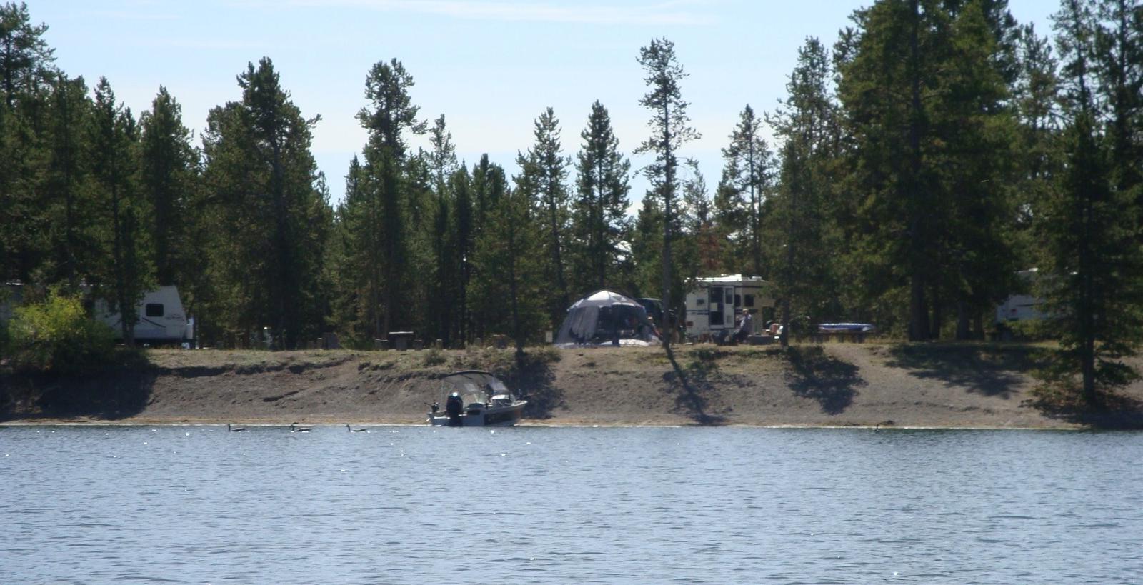 View from Hebgen Lake - Lake, boat and RV surrounded by pine treesLonesomehurst Campground
