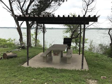 Covered picnic table, grill, and fire ring at site with Waco Lake in the background