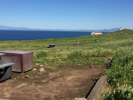 Picnic table and metal food storage box on terrace overlooking ocean, two buildings and lighthouse. ANACAPA ISLAND AREA - 006
