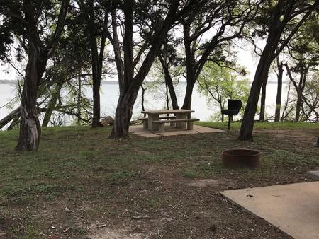 Picnic table, grill, and fire ring at site with Waco Lake in the background