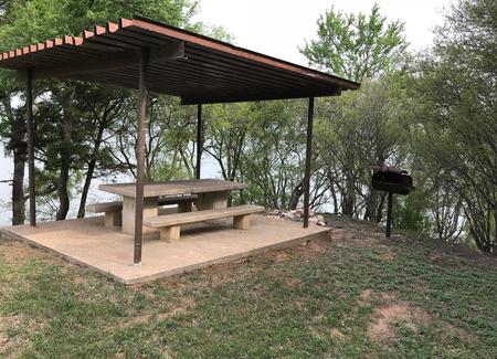 RV site with covered picnic table, grill, and Waco Lake in the background