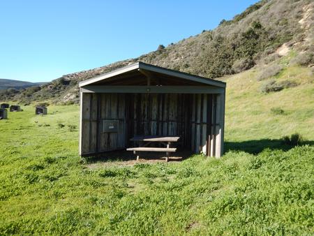 Eight foot tall wind shelter with picnic table surrounded by green grass. Sites 001-015 - 001
