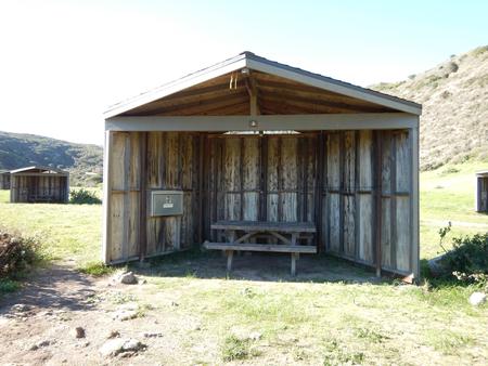 Eight foot tall wind shelter with picnic table surrounded by green grass. Sites 001-015 - 002
