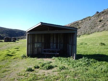 Eight foot tall wind shelter with picnic table surrounded by green grass. Sites 001-015 - 003
