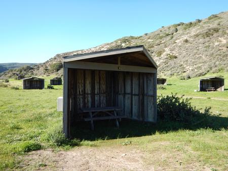 Eight foot tall wind shelter with picnic table surrounded by green grass. Sites 001-015 - 005
