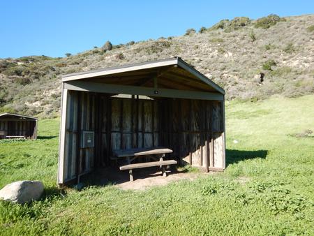 Eight foot tall wind shelter with picnic table surrounded by green grass. Sites 001-015 - 006
