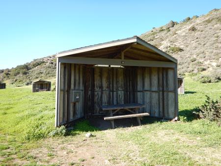Eight foot tall wind shelter with picnic table surrounded by green grass. Sites 001-015 - 008
