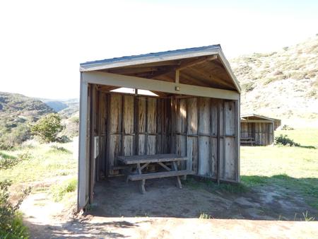 Eight foot tall wind shelter with picnic table surrounded by green grass. Sites 001-015 - 009
