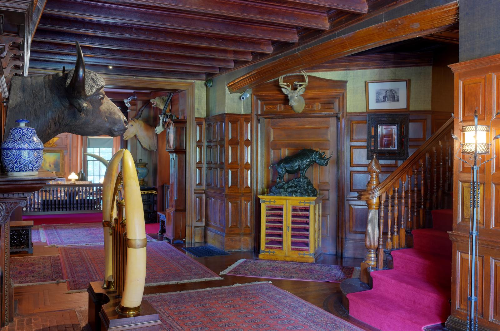 A hall wall with hunting trophies, oak paneled walls, and a staircase.