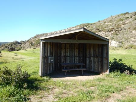 Eight foot tall wind shelter with picnic table surrounded by green grass. Sites 001-015 - 011
