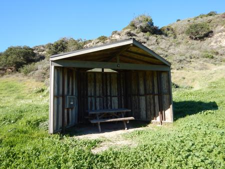 Eight foot tall wind shelter with picnic table surrounded by green grass. Sites 001-015 - 014
