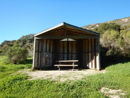 Eight foot tall wind shelter with picnic table surrounded by green grass. Sites 001-015 - 015
