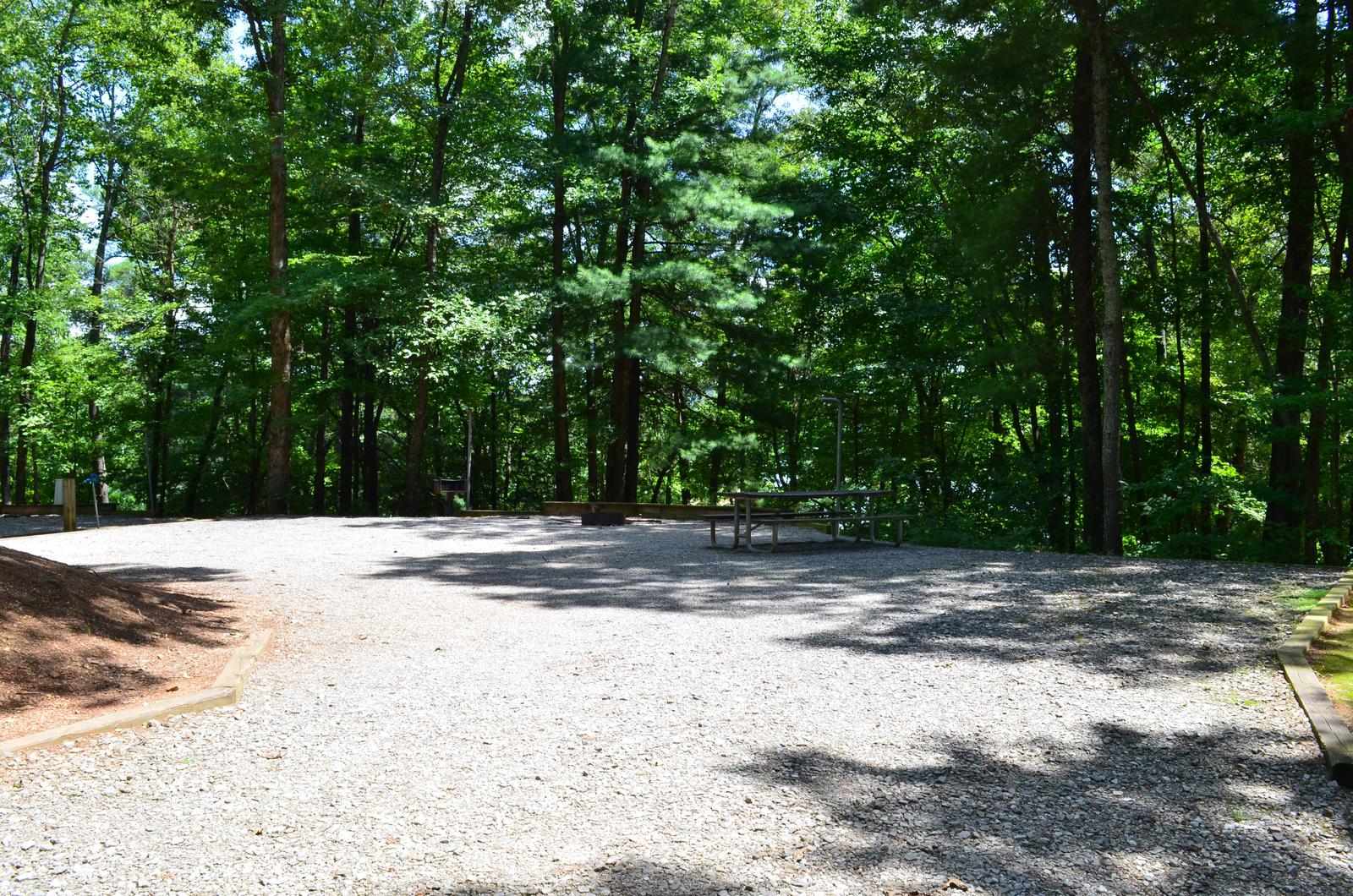 Round gravel site with dense tree coverage and table, grill, fire pit Large gravel site with fire pit, grill, table 