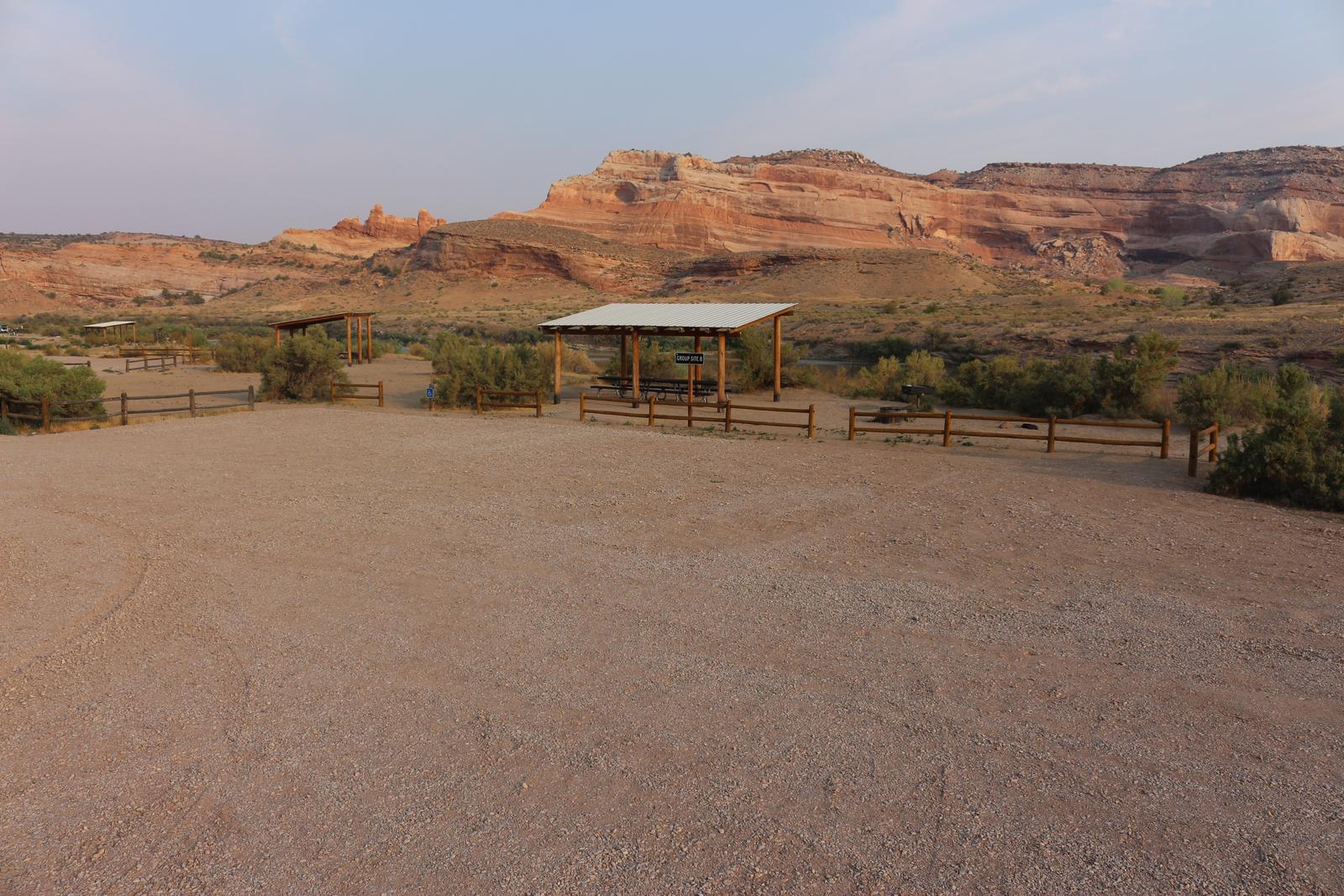Dewey Bridge Group Site B large parking area with the Dewey Bridge Group Site B large parking area with the shade shelter and picnic tables in the near distance. Red rock cliffs line the horizon. shelter and picnic tables in the near distance.Dewey Bridge Group Site B large parking area with the shade shelter and picnic tables in the near distance. Red rock cliffs line the horizon. 