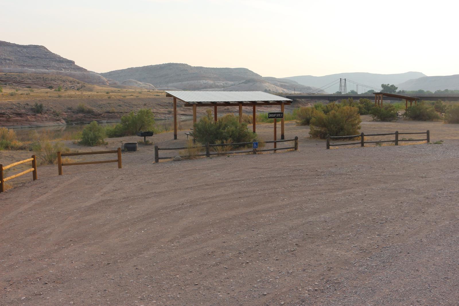Dewey Bridge Group Site C parking area, picnic tables, and shade shelter. The historic Dewey Bridge in the distance. 