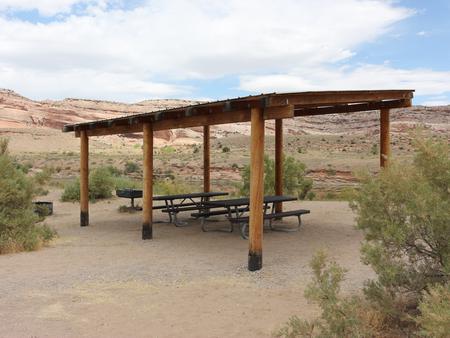 Dewey Bridge Group Site C shade shelter and picnic tables. Rolling red rock cliffs in the distance. 