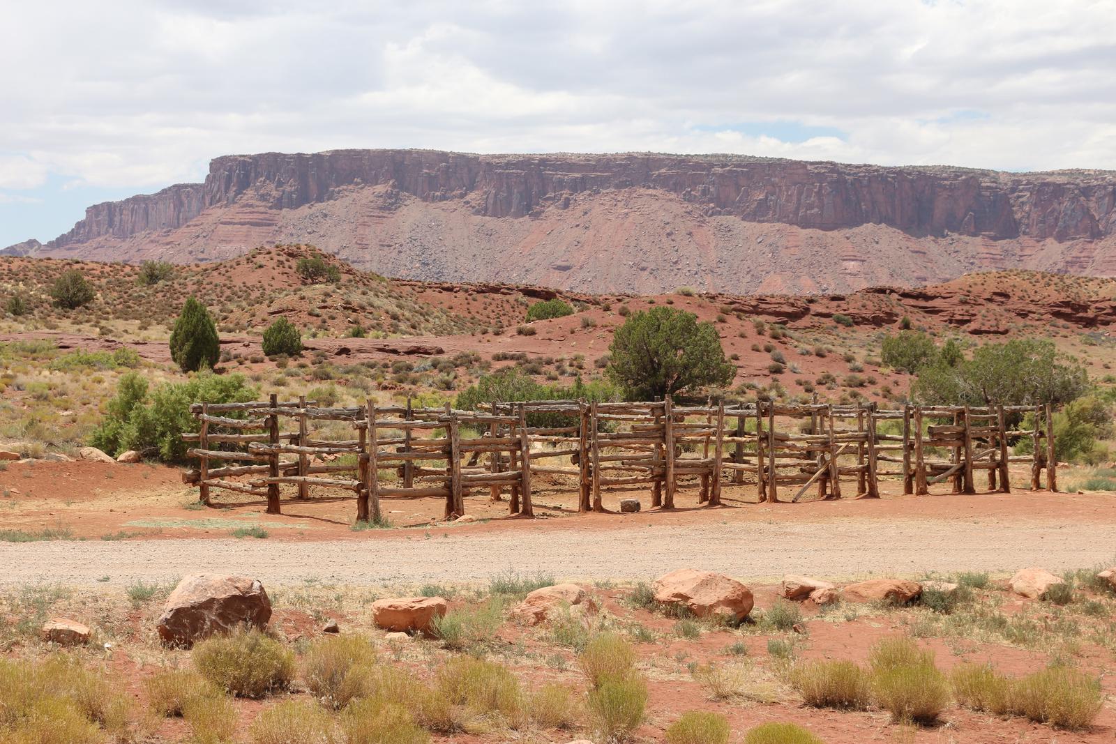 The horse corral at Upper Onion Creek Group Site A is a rail fence. It is located right next to the access road to the site. In the distance are the tall plateaus that surround Fisher Valley.