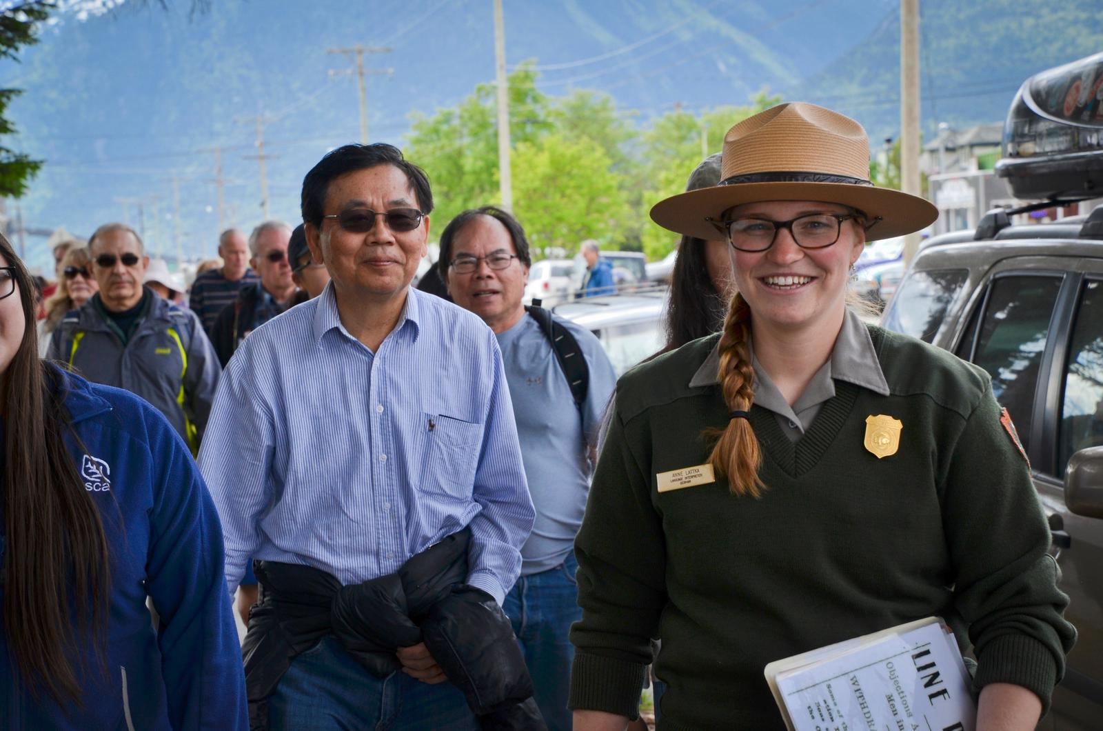 A ranger smiles at the camera with tour group walking behind.
