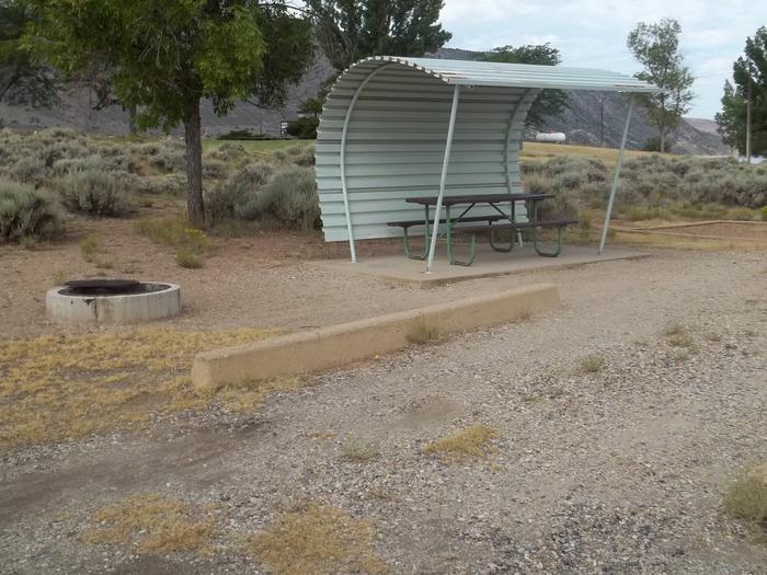 Picnic table with shelter on one side and overhead and a firepit located to the side of the picnic area.Antelope Flat Campground: Site 3