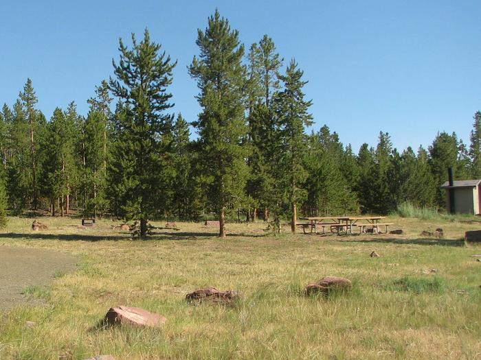 Picnic tables in a semi-grassy area with the restrooms off to the side.Browne Lake Campground: Group Site 1