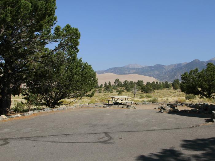 View of Site #67 parking pad and tent site, with picnic table and fire ring. Mountains and Sand Dunes can be seen in the background.Site #67, Pinon Flats Campground
