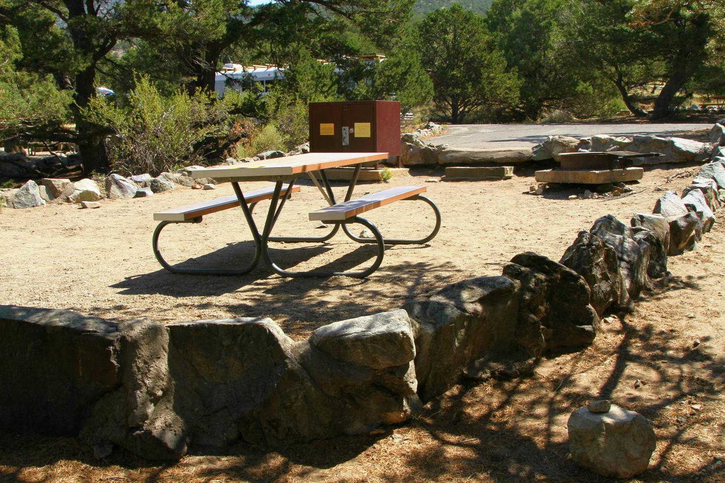 Close up of Site #78 tent pad with picnic table, bear box, and fire ring. Tent pad is bordered by a low rock wall.Site #78, Pinon Flats Campground