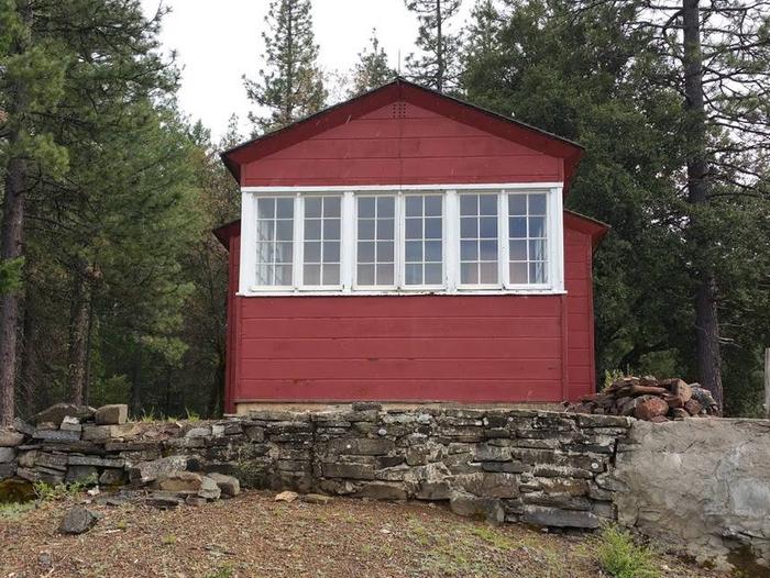 Back view of historic Post Creek Guard Station, red cabin, with white trim around windows.This is the view of the cabin from the back. These windows look out over several mountain ridgelines offering guests beautiful views.