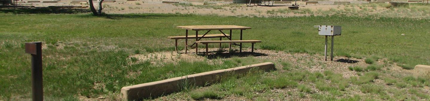 Picnic table and grill in a semi grassy area.Buckboard Crossing Campground: Loop B, Site 10