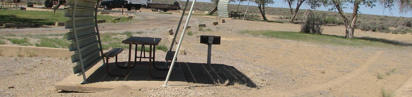 Partially covered picnic table on a slab of cement with a grill off to the side in the gravel.Buckboard Crossing Campground: Loop B, Site 13