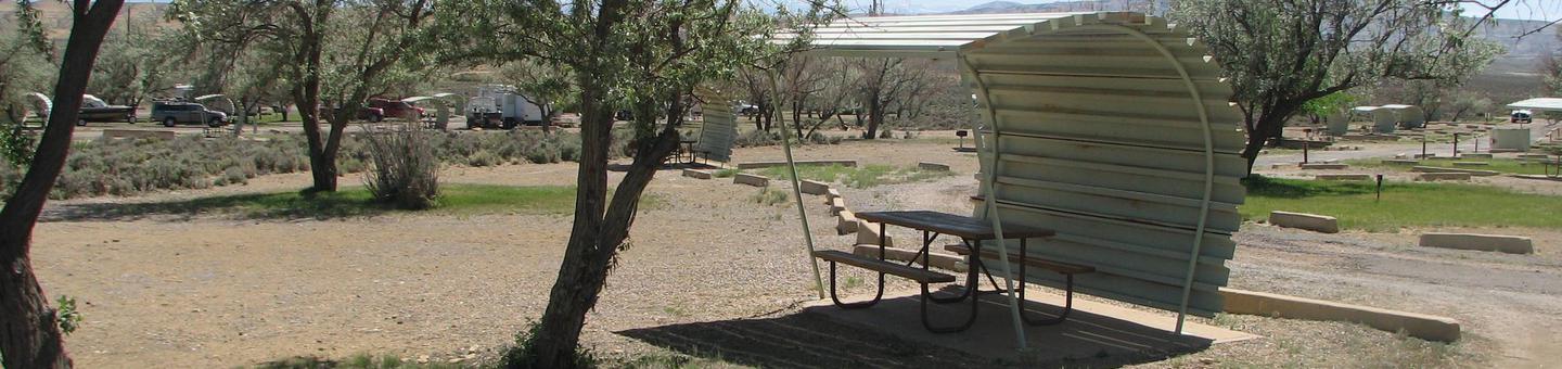 Partially covered picnic table on a slab of cement in a gravel area.Buckboard Crossing Campground: Loop B, Site 14