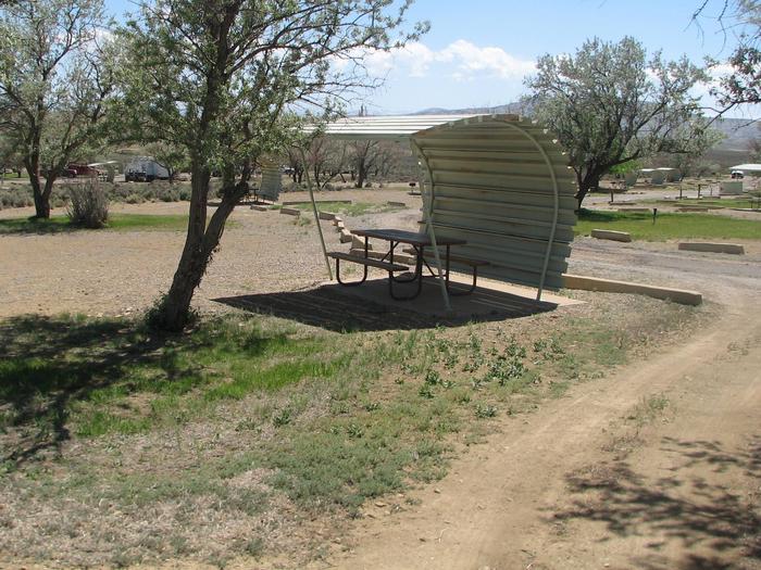 Partially covered picnic table on a slab of cement in a gravel area. Parking location is on the side of the picnic table.Buckboard Crossing Campground: Loop B, Site 14