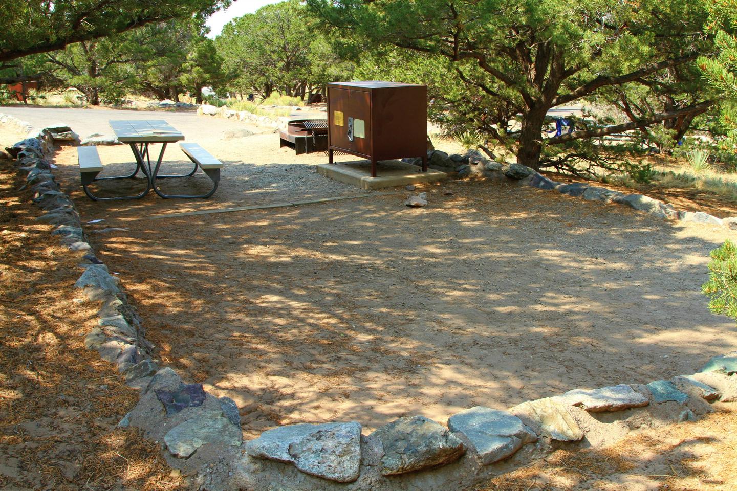 Back view of Accessible Site #63 tent pad, with picnic table, bear box, and fire ring. Shows low rock wall on border of site.Site #63, Pinon Flats Campground