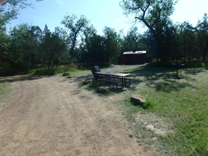 In the foreground is the picnic table and a trashcan with pit toilets in the background.  These pit toilets are the only accessible toilets in the campground. This accessible site is near the pit toilets. Please note people make walk through site. 