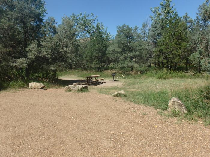 Site 11 is lined with large boulders on the edge closest to the picnic table and grill which are in the background of the photo with the gravel pad in the foreground. Site 11, as this is a left hand pull through the picnic table will not be on the same side as RV doors. 