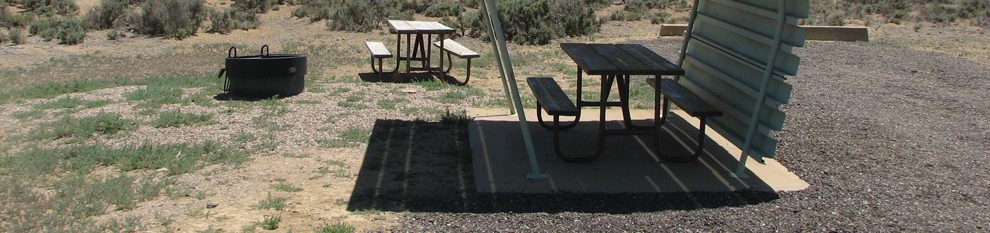Partially covered picnic table on a slab of cement and a fire pit and picnic table in a mostly graveled area.Buckboard Crossing Campground: Loop A, Site 2