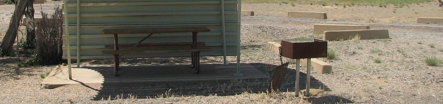 This site has a partially covered picnic table on a slab of cement with a grill next to it held up by a metal rod in the ground.Buckboard Crossing Campground: Loop B, Site 2