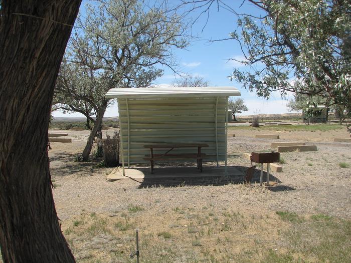 This site has a partially covered picnic table on a slab of cement with a grill next to it held up by a metal rod in the ground.Buckboard Crossing Campground: Loop B, Site 2