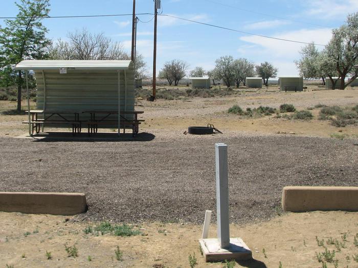 This site has two partially covered picnic table on a slab of cement and a fire pit found in the gravel. There are a number of other sites in the background.Buckboard Crossing Campground: Loop A, Site 24