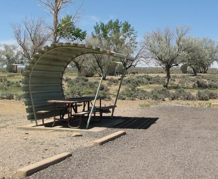 This site has two partially covered picnic table on a slab of cement and a fire pit found in the gravel. Buckboard Crossing Campground: Loop A, Site 24