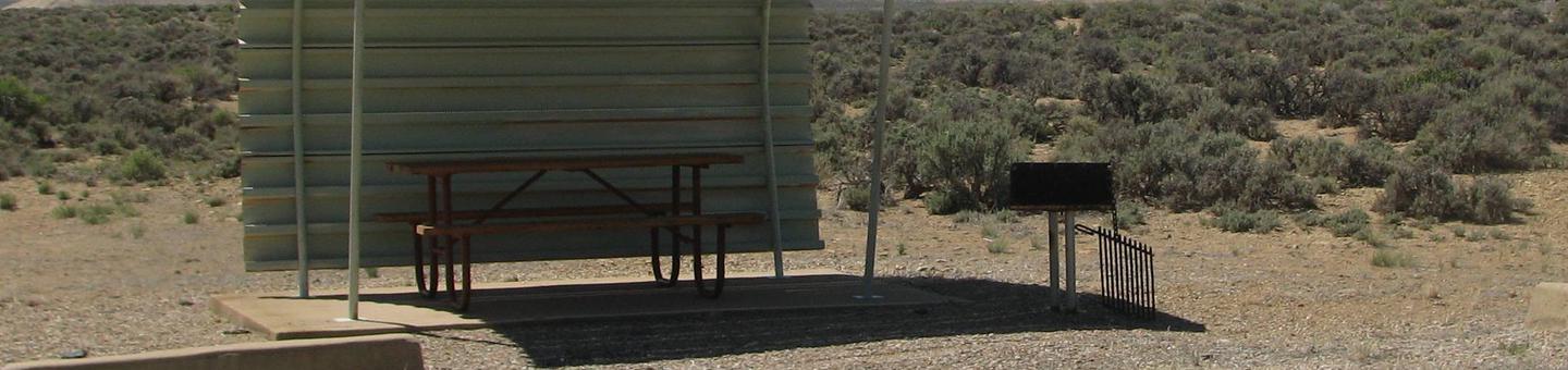 This site has a partially covered picnic table on a slab of cement with a grill next to it held up by a metal rod in the ground.Buckboard Crossing Campground: Loop B, Site 24